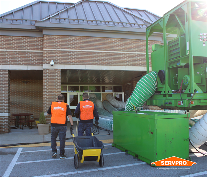 Two technicians in orange vests walking into a school next to a big, green desiccant dehumidifier 